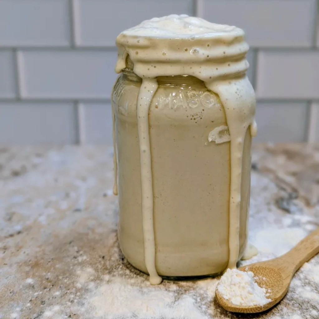 Active, bubbly sourdough starter fermenting in a clear glass jar, showing how to make sourdough starter from scratch